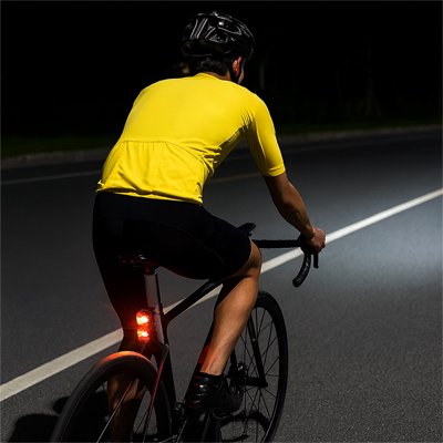 Cycliste en maillot jaune avec feu arrière allumé sur route nocturne